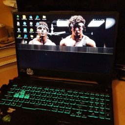 BartekDera.pl - Usługi Informatyczne i Edukacja mgr inż. Bartłomiej Dera - Czarny laptop z podświetlaną na zielono klawiaturą, na ekranie widoczny kadr z filmu z Sylwestrem Stallone i Carlem Weathersem, na obudowie naklejki.