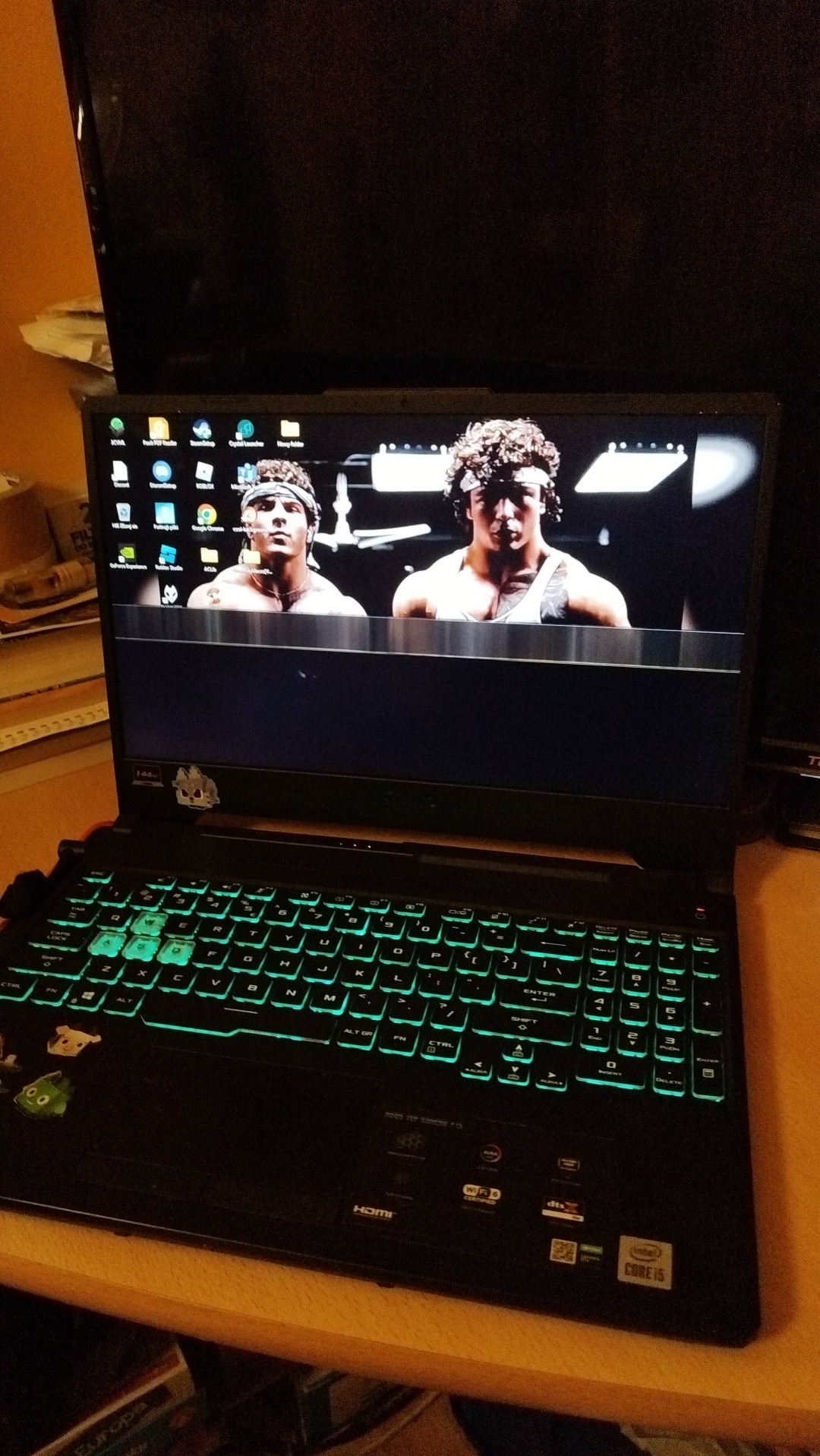 Czarny laptop z podświetlaną na zielono klawiaturą, na ekranie widoczny kadr z filmu z Sylwestrem Stallone i Carlem Weathersem, na obudowie naklejki.