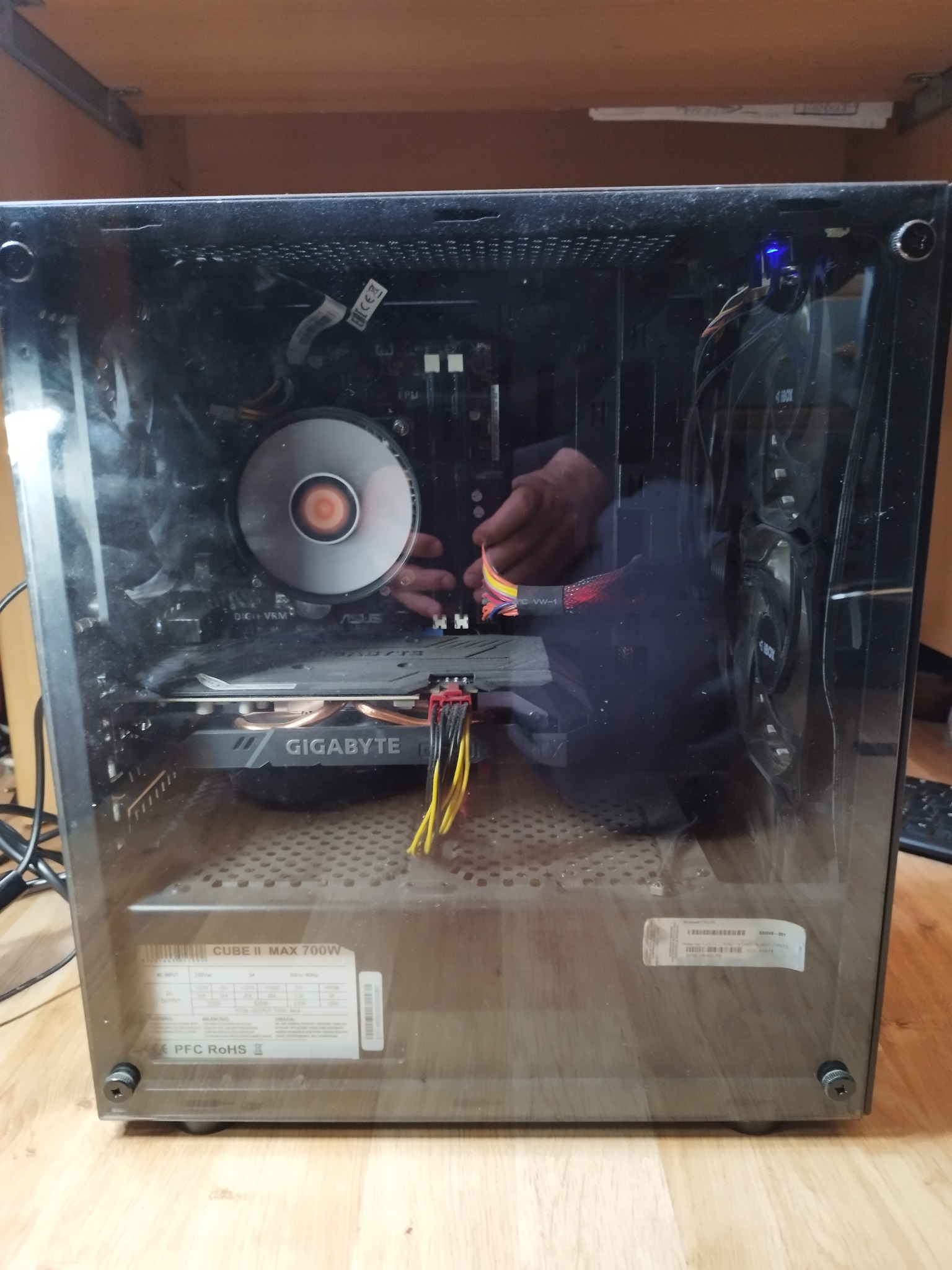 Wnętrze obudowy komputera stacjonarnego z widoczną kartą graficzną Gigabyte, chłodzeniem procesora Asus i zasilaczem Cube II Max 700W, podczas podłączania przewodów.