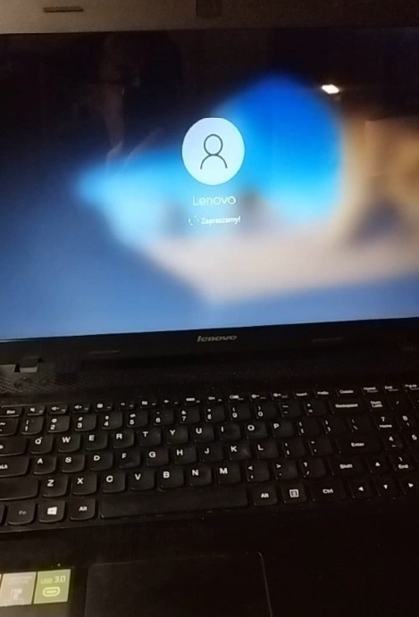 Ekran logowania laptopa Lenovo z widoczną ikoną użytkownika i napisem 'Zapraszamy!', klawiatura w dolnej części kadru.