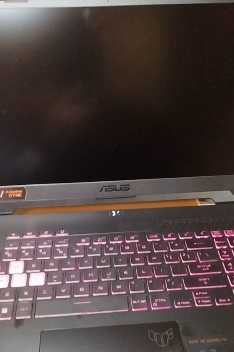 Otwarty laptop ASUS TUF Gaming F15 z podświetlaną klawiaturą na różowo, widoczne logo ASUS i Adaptive Sync, ekran wyłączony.
