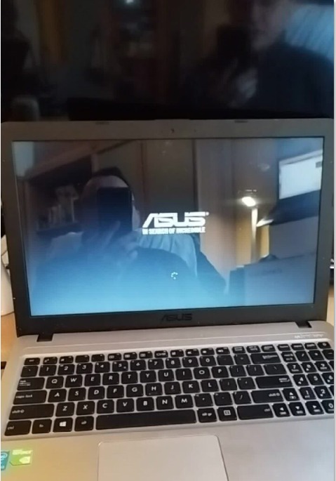 Laptop marki ASUS w trakcie uruchamiania systemu, widoczny ekran startowy z logo firmy, na tle odbicie osoby; usługa w Międzychodzie.