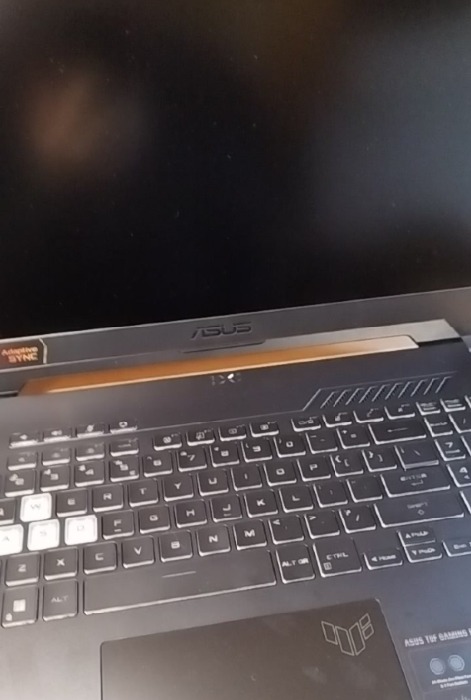 Częściowy widok laptopa ASUS TUF Gaming z podświetlaną klawiaturą, widoczny napis Adaptive Sync i logo TUF na touchpadzie.