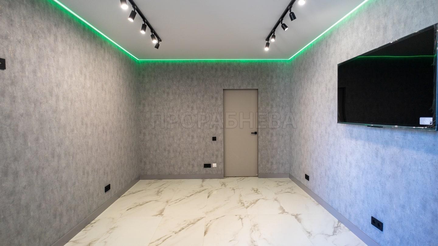 Pokój po remoncie: szare ściany z fakturą, biała marmurowa podłoga, oświetlenie LED, czarne reflektory, telewizor na ścianie, beżowe drzwi. Nowoczesne wykończenie wnętrza.