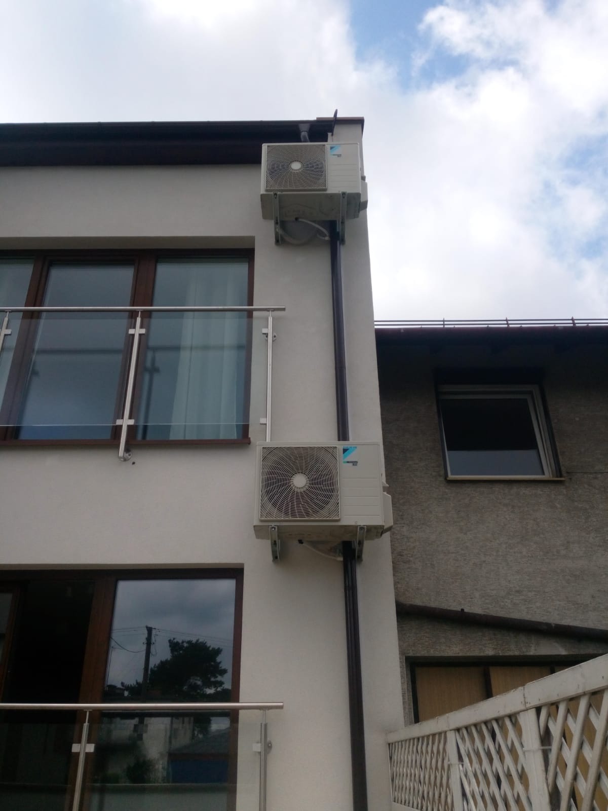 Dwa klimatyzatory marki Daikin zamontowane na elewacji budynku mieszkalnego obok okien z brązowymi ramami i szklaną balustradą balkonu.