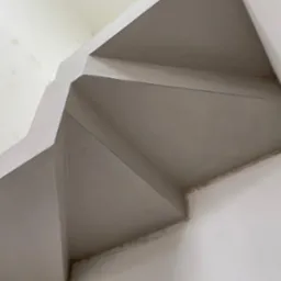 Gładka, szara powierzchnia świeżo nałożonego tynku na skosach sufitu i ścian, widoczne łączenia i niedoskonałości w narożnikach.