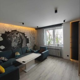 R&J - WYKOŃCZENIA - Salon z szarą podłogą z paneli, narożnikiem w odcieniach niebieskiego, fototapetą z motywem tygrysa i oświetleniem LED nad nią.