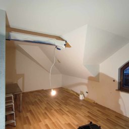 R&J - WYKOŃCZENIA - Pokój na poddaszu w trakcie przygotowań do malowania: zabezpieczona taśmą krawędź sufitu, widoczne fragmenty listew przypodłogowych, drewniana podłoga panelowa i wisząca żarówka.