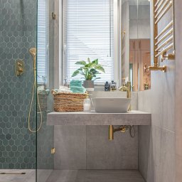 Ewa Musialik-Sojka Out-In - Nowoczesna łazienka z kabiną prysznicową wykończoną turkusową mozaiką w kształcie rybiej łuski, umywalką nablatową, złotą armaturą i grzejnikiem drabinkowym, uzupełniona o wiklinowy koszyk...