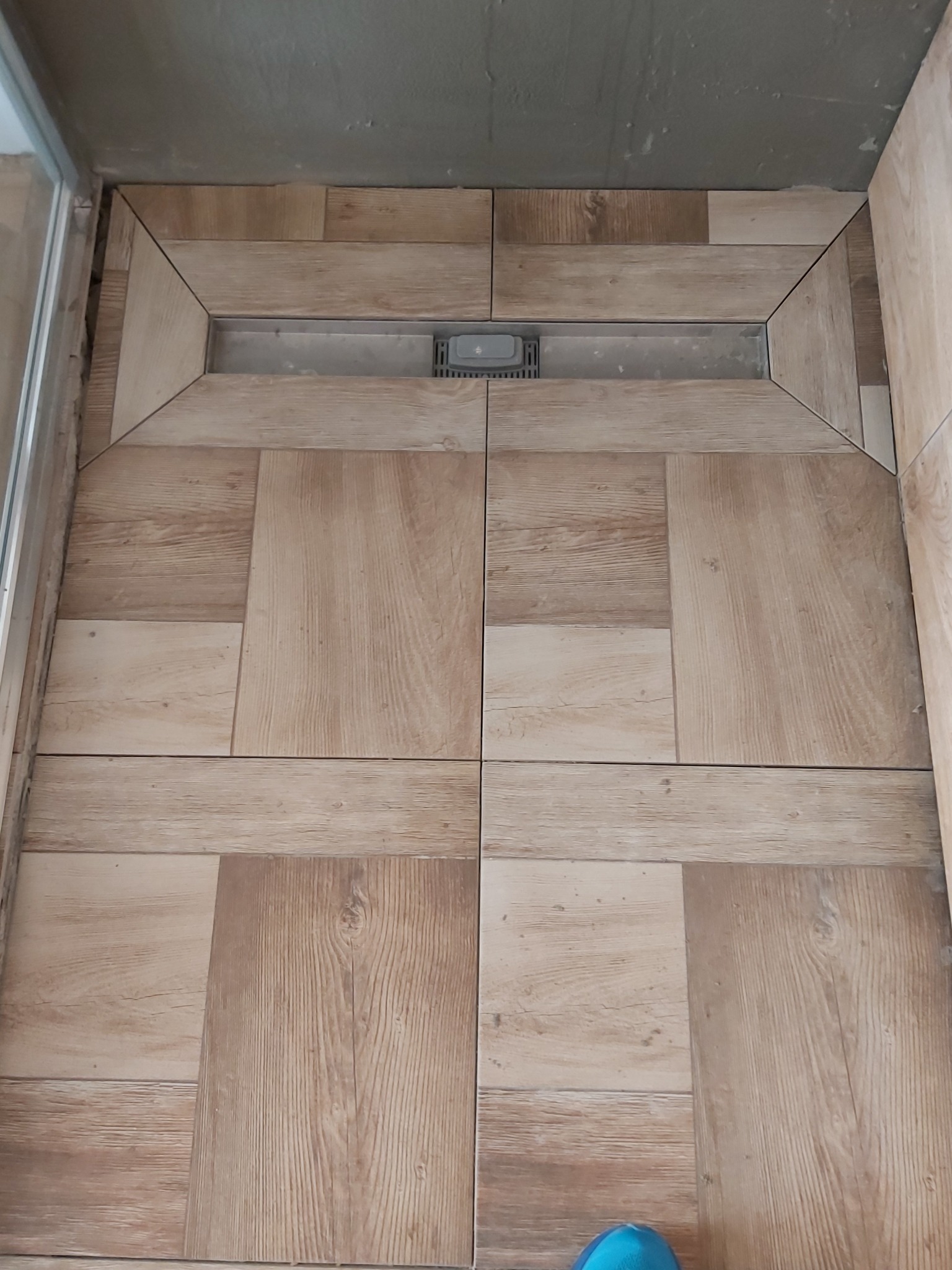 Ułożone płytki podłogowe imitujące drewno w kabinie prysznicowej z odpływem liniowym.