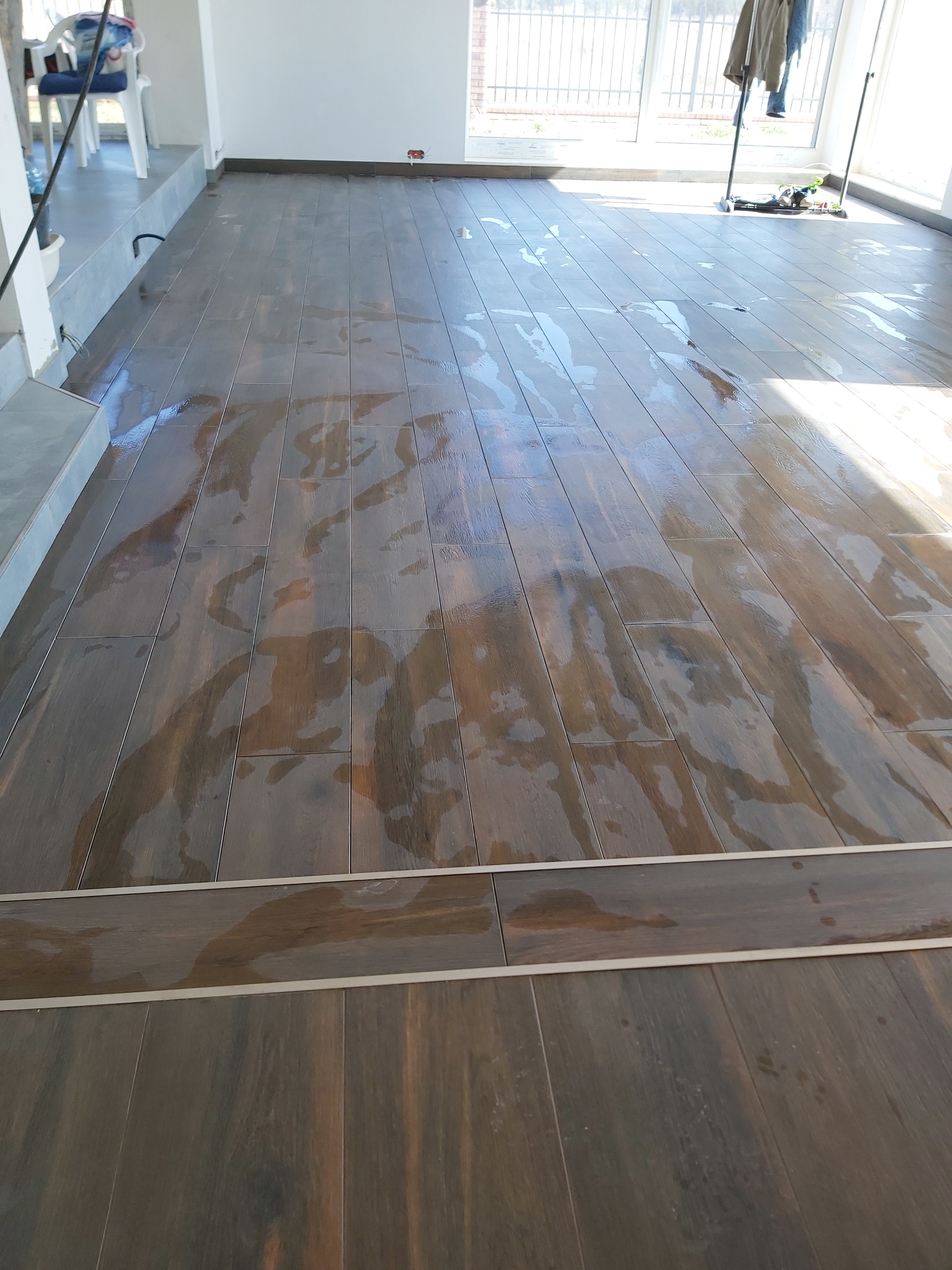 Świeżo ułożona, mokra podłoga z paneli w odcieniach brązu w jasnym pomieszczeniu w Warszawie, widoczne ślady wody po czyszczeniu.