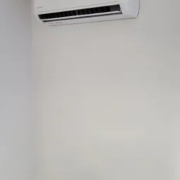 Biała klimatyzacja TATA zamontowana na białej ścianie, wyświetlacz pokazuje temperaturę 16 stopni, widoczna rura na g&oacute;rze po prawej stronie.