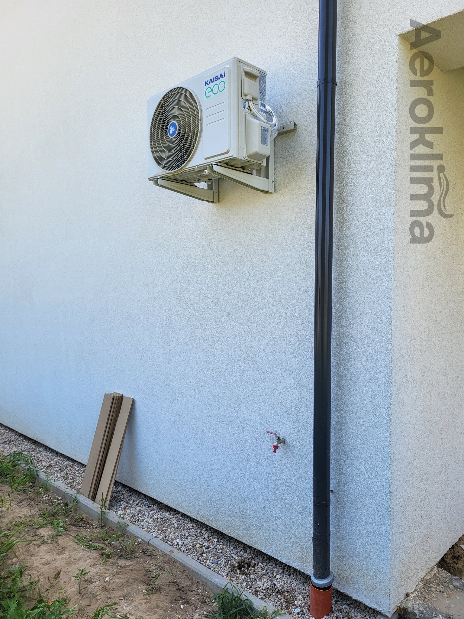 Zewnętrzna jednostka klimatyzacji Kaisai ECO zamontowana na jasnej ścianie budynku, obok rury spustowej, z widocznym logo firmy Aeroklima po prawej stronie.