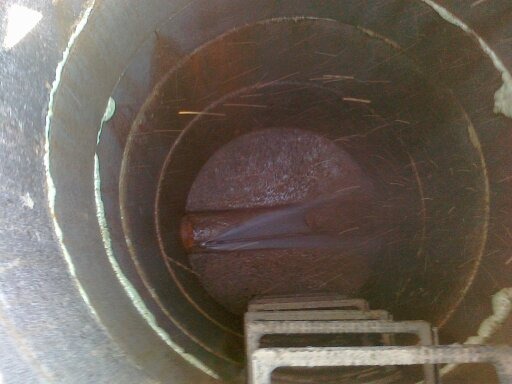 Wnętrze betonowej studni kanalizacyjnej z drabinką, widoczny wypływający strumień wody.