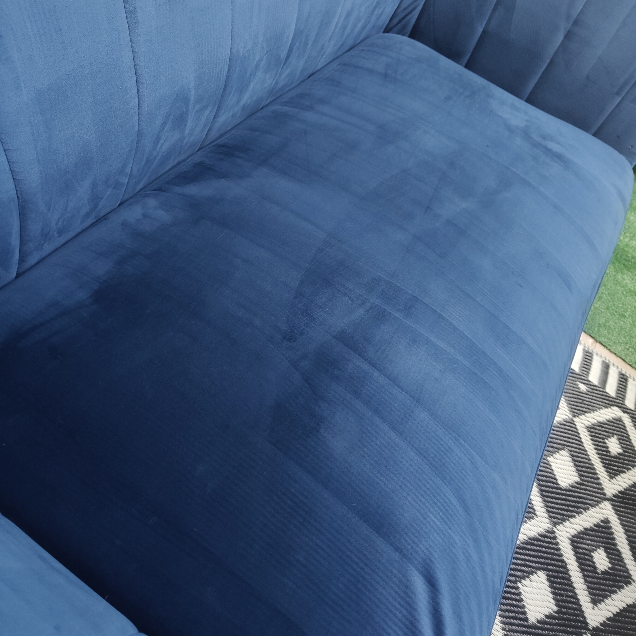Wyprana, niebieska, welurowa sofa z widocznymi śladami po czyszczeniu, na tle dywanu w Głogowie. Widoczne delikatne prążki na materiale.