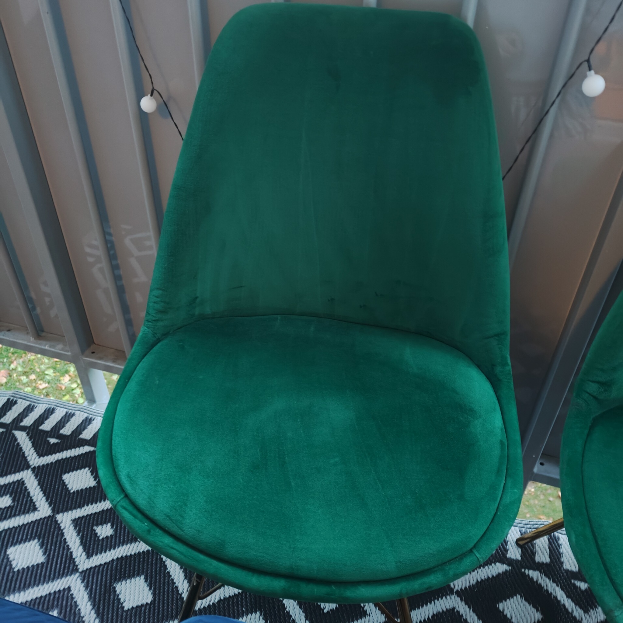 Szmaragdowe krzesło z weluru na balkonie z geometrycznym dywanem, oświetlone girlandą żarówkową, widziane z góry.