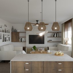 Aleksandra Brzozowicz KOMPOZYCJA STUDIO - Salon z wyspą kuchenną w stylu boho: drewniane szafki, rattanowe lampy, jasne sofy, galeria zdjęć na ścianie, telewizor na tle kamiennej ściany. Przytulne i stylowe wnętrze.