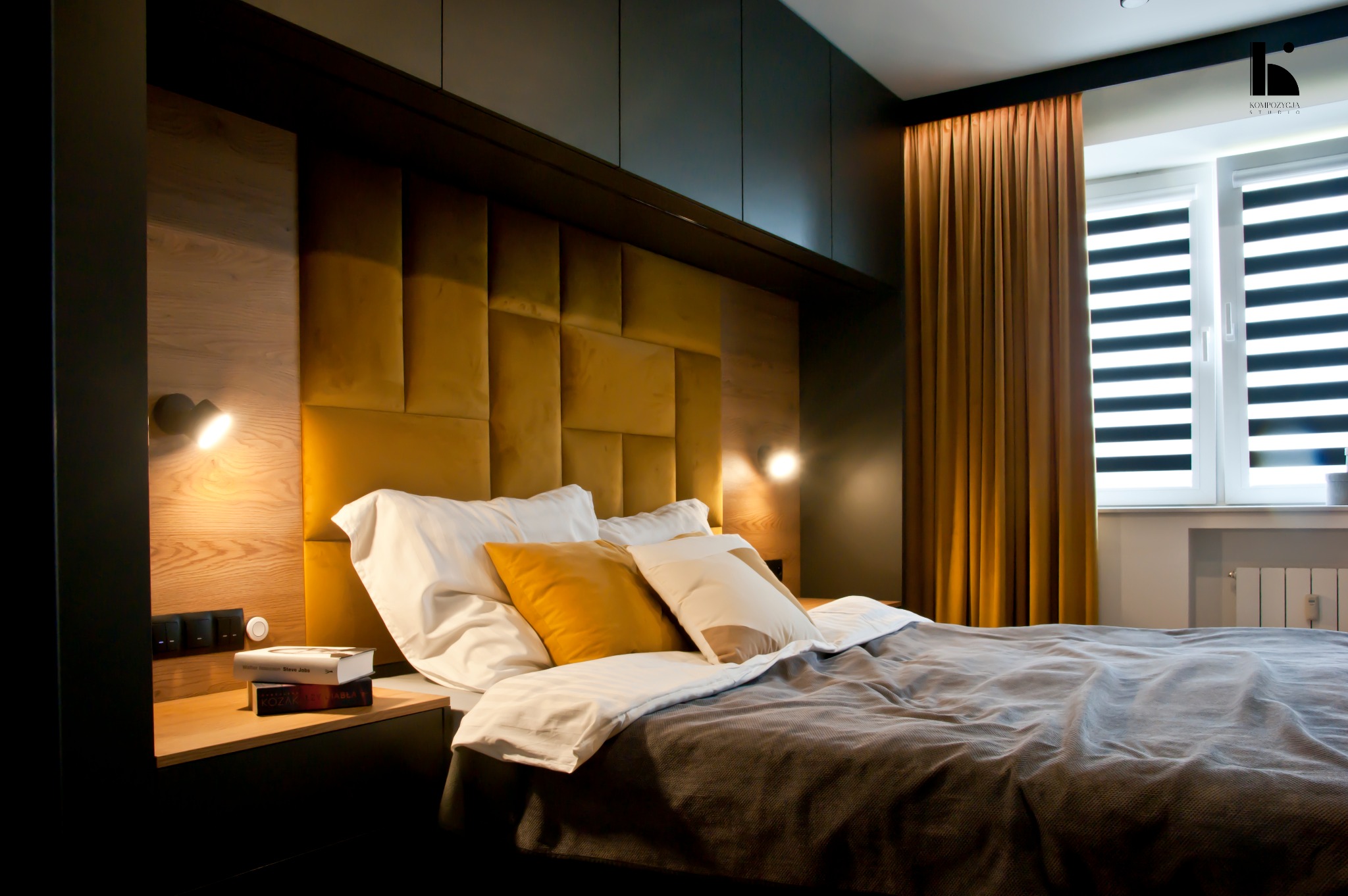 Nowoczesna sypialnia z łóżkiem z żółtym, pikowanym zagłówkiem, drewnianą boazerią, czarnymi szafkami i zasłonami w kolorze musztardowym.