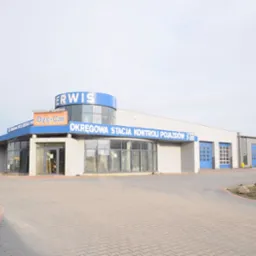 Budynek Okręgowej Stacji Kontroli Pojazdów Dyce-Car z widocznym wejściem i bramami garażowymi, znak 'Wjazd' na trawniku.