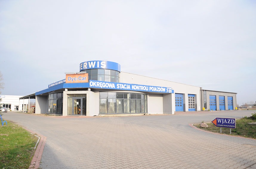 Budynek Okręgowej Stacji Kontroli Pojazdów Dyce-Car z widocznym wejściem i bramami garażowymi, znak 'Wjazd' na trawniku.