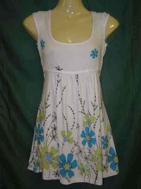 Biała tunika damska z motywem niebiesko-zielonych kwiatów na manekinie bez głowy, z kwadratowym dekoltem i marszczeniem pod biustem.