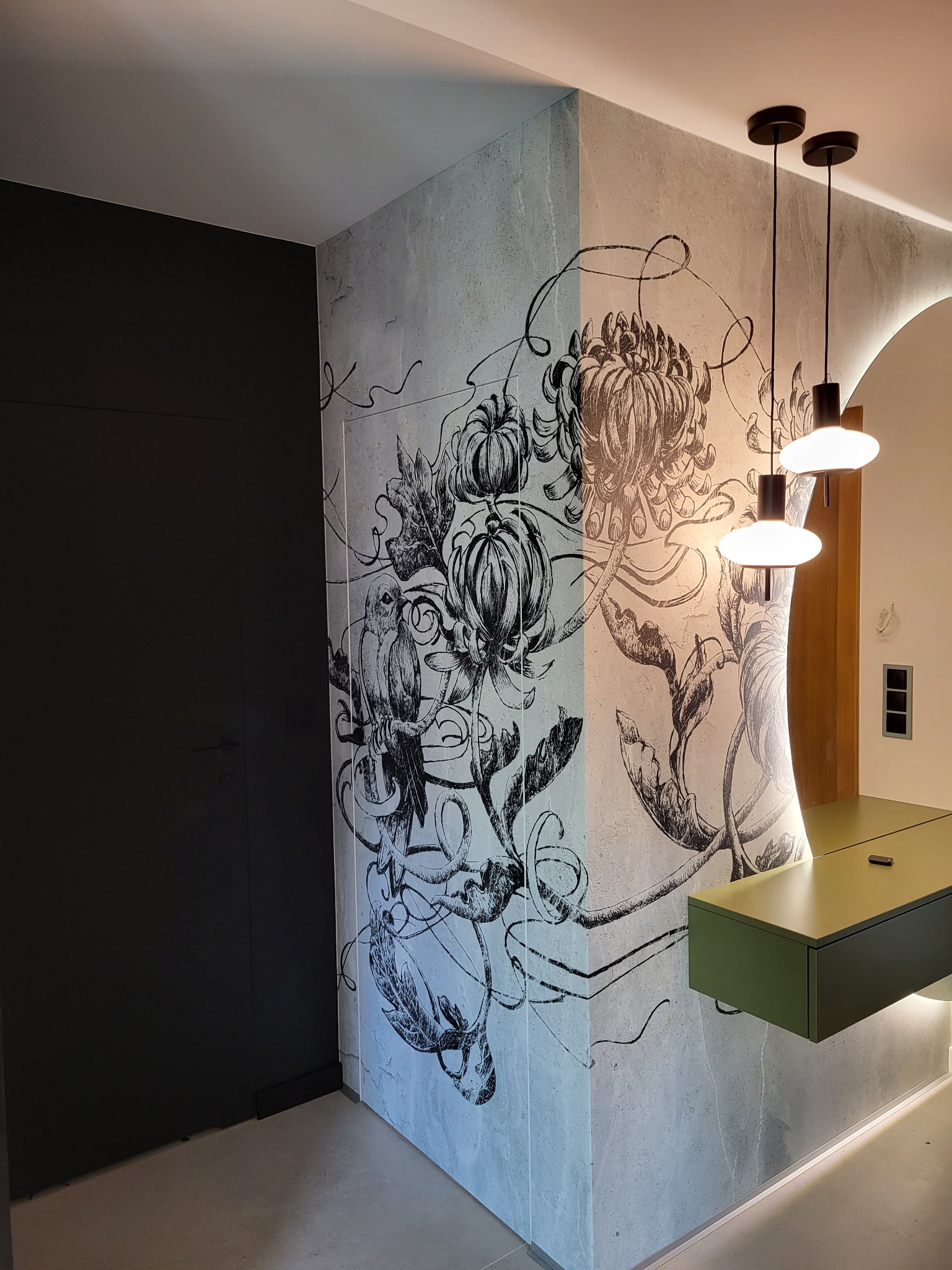 Wykończona ściana z motywem kwiatowym i ptasim, oświetlona lampami wiszącymi i podświetleniem LED. Nowoczesny design wnętrza z elementami dekoracyjnymi.