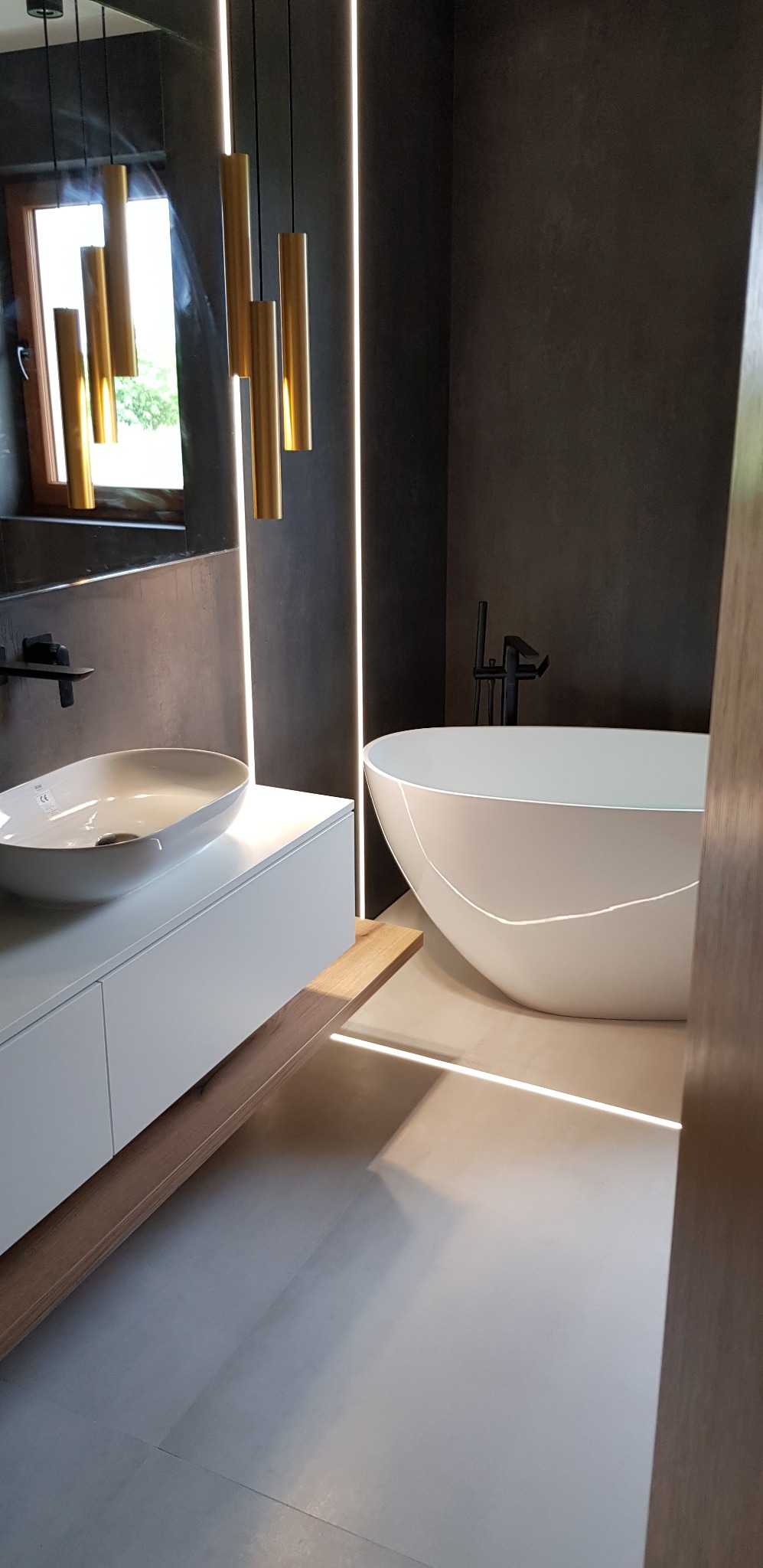 Nowoczesna łazienka z wolnostojącą wanną, umywalką nablatową i oświetleniem LED. Minimalistyczny design z ciemnymi ścianami i jasną podłogą.