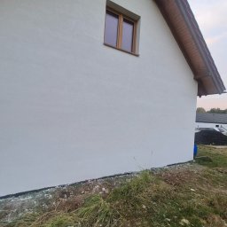 FIRMA USŁUGOWA - Boczny widok domu z białą elewacją, drewnianym oknem i dachem z drewnianą podbitką, trawa i gruz przy fundamencie.