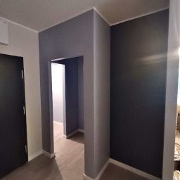 BudService Vasyl Kretsul - Pomieszczenie po malowaniu w Poznaniu. Ciemne ściany w odcieniach szarości, drewniana podłoga, białe listwy przypodłogowe i framugi drzwi.