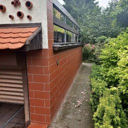 BudService Vasyl Kretsul - Ceglana elewacja budynku z tarasem i elementami dekoracyjnymi, widok z zewnątrz. Czerwona cegła z jasną fugą i drewniane elementy wykończeniowe.