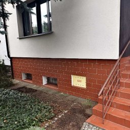 BudService Vasyl Kretsul - Elewacja domu z oknem, czerwoną cegłą klinkierową w dolnej części i schodami wejściowymi. Tabliczka gazowa na ścianie.