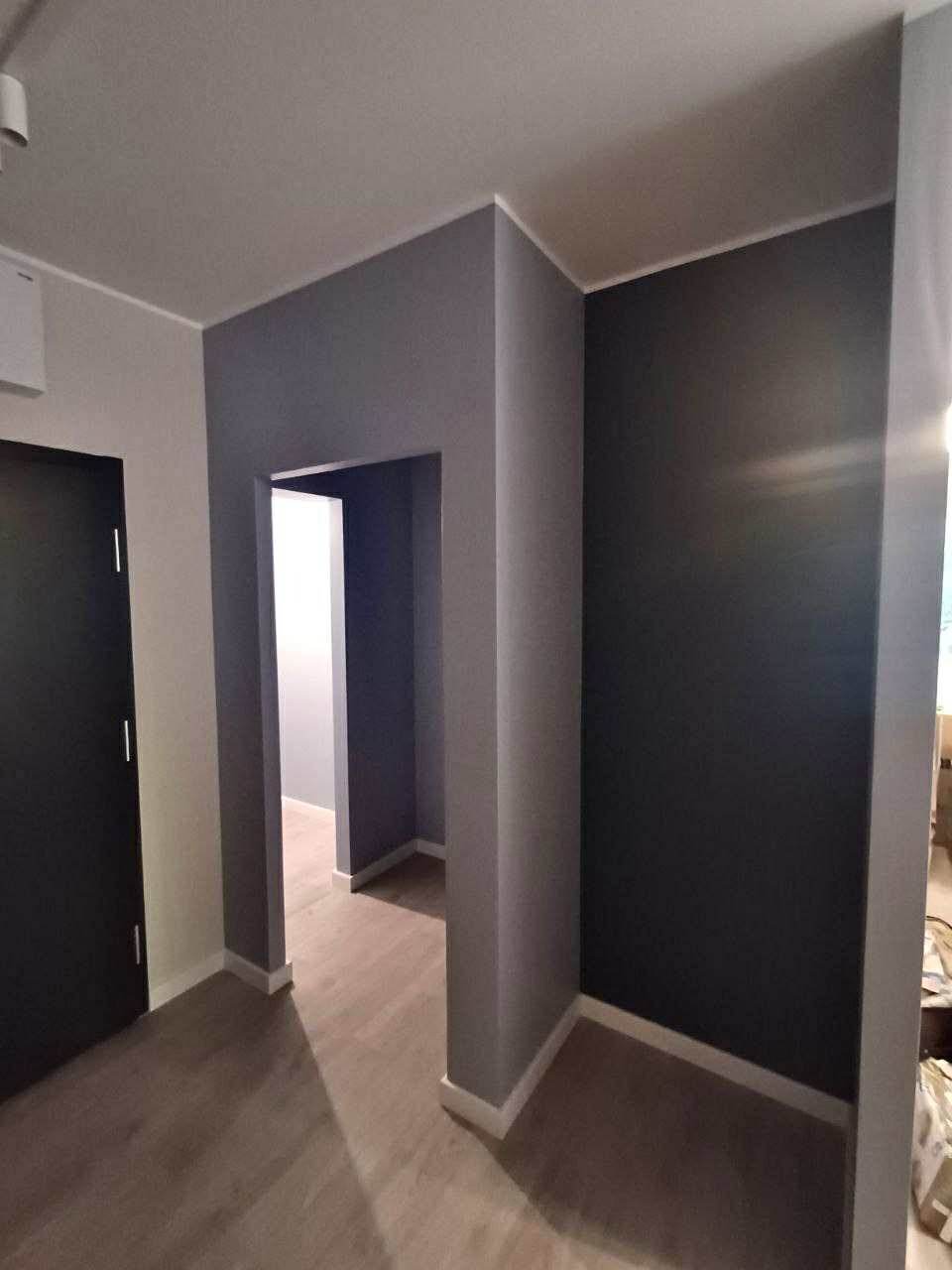 Pomieszczenie po malowaniu w Poznaniu. Ciemne ściany w odcieniach szarości, drewniana podłoga, białe listwy przypodłogowe i framugi drzwi.