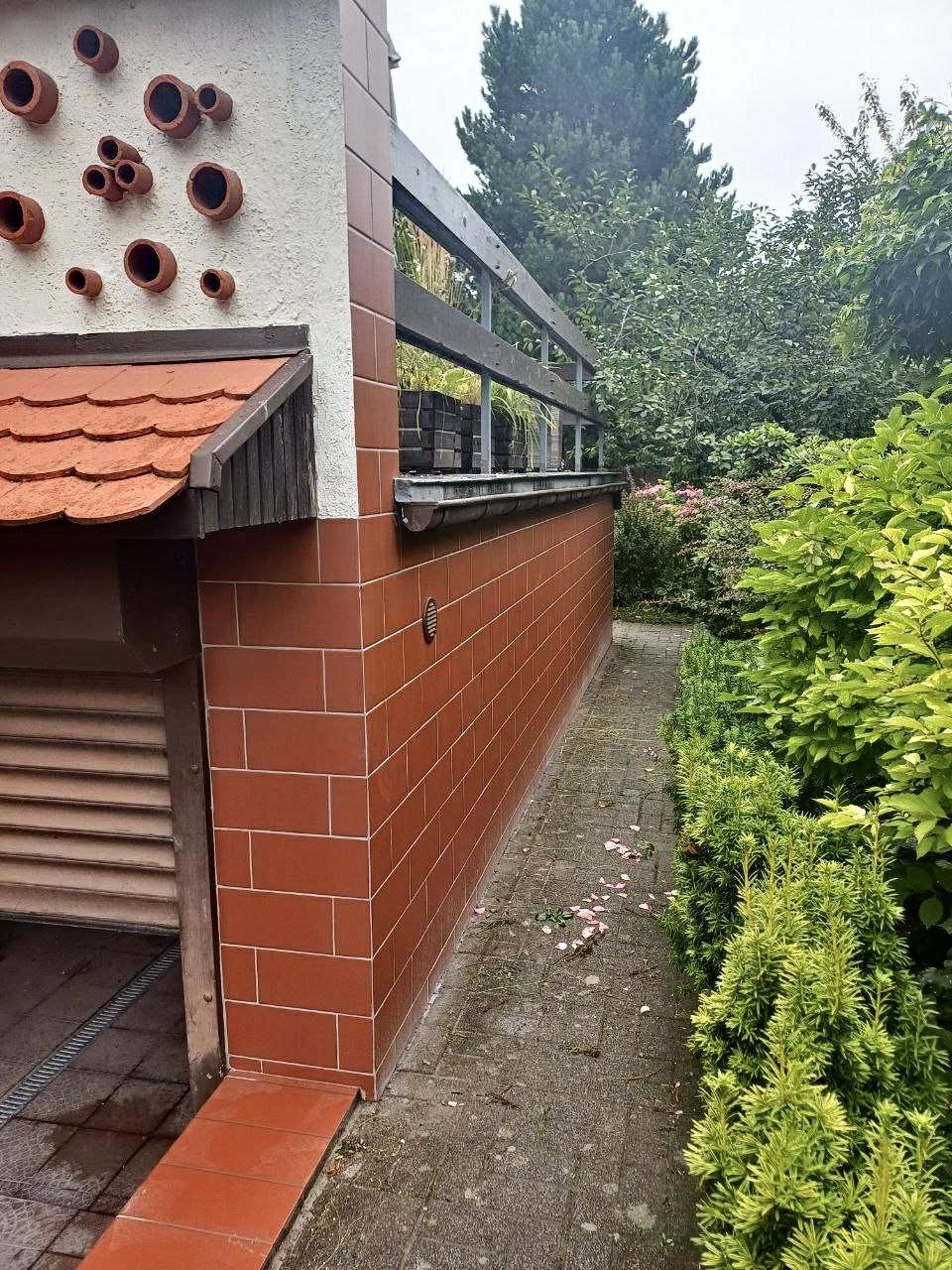 Ceglana elewacja budynku z tarasem i elementami dekoracyjnymi, widok z zewnątrz. Czerwona cegła z jasną fugą i drewniane elementy wykończeniowe.