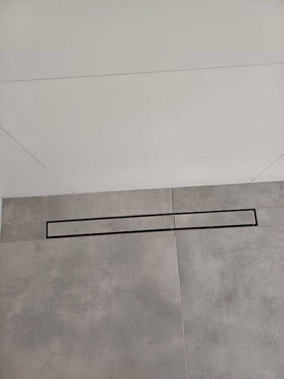 Szara, matowa glazura podłogowa z czarnym odpływem liniowym w kabinie prysznicowej. Minimalistyczny design łazienki, nowoczesne wykończenie.