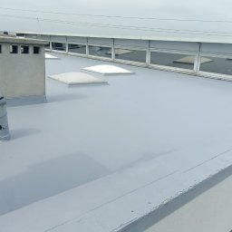 M&M Mariusz Sitek - Szary dach pokryty jednolitą, gładką powłoką, z elementami wentylacyjnymi i świetlikami, widoczne okna budynku w tle.