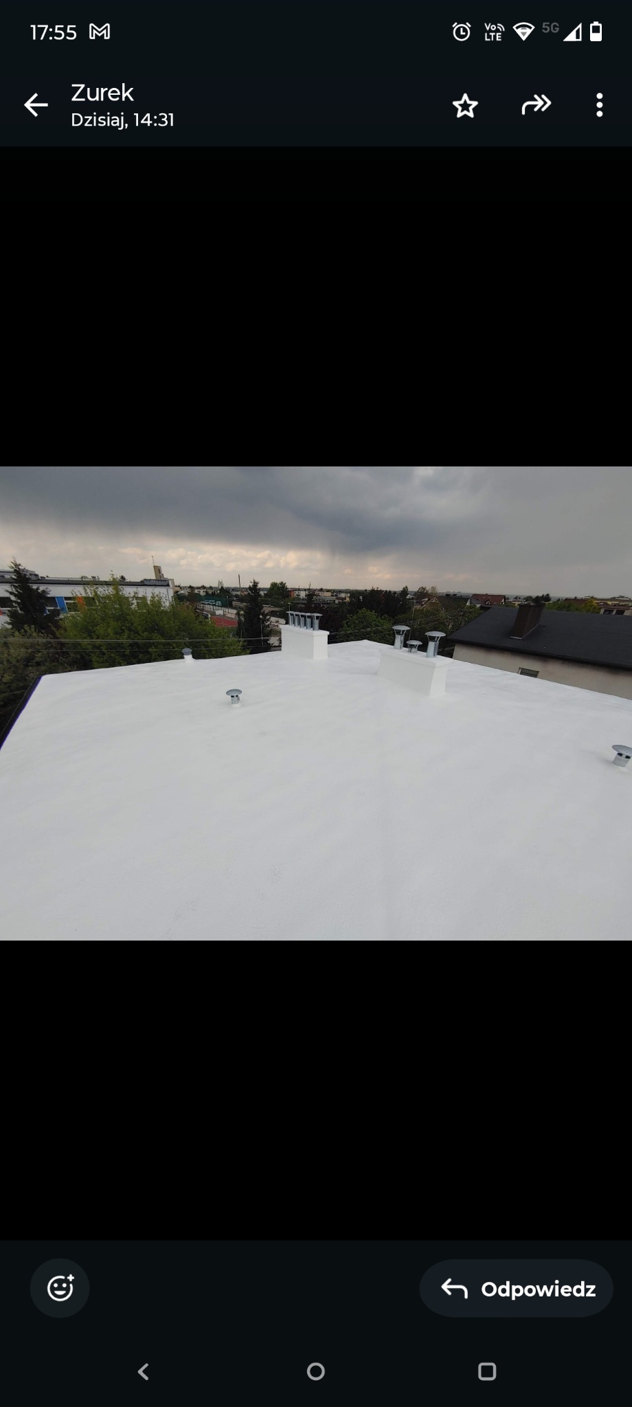 Biały, płaski dach po renowacji z widocznymi kominami wentylacyjnymi na tle zabudowań miejskich pod pochmurnym niebem. Nowoczesna izolacja dachu.