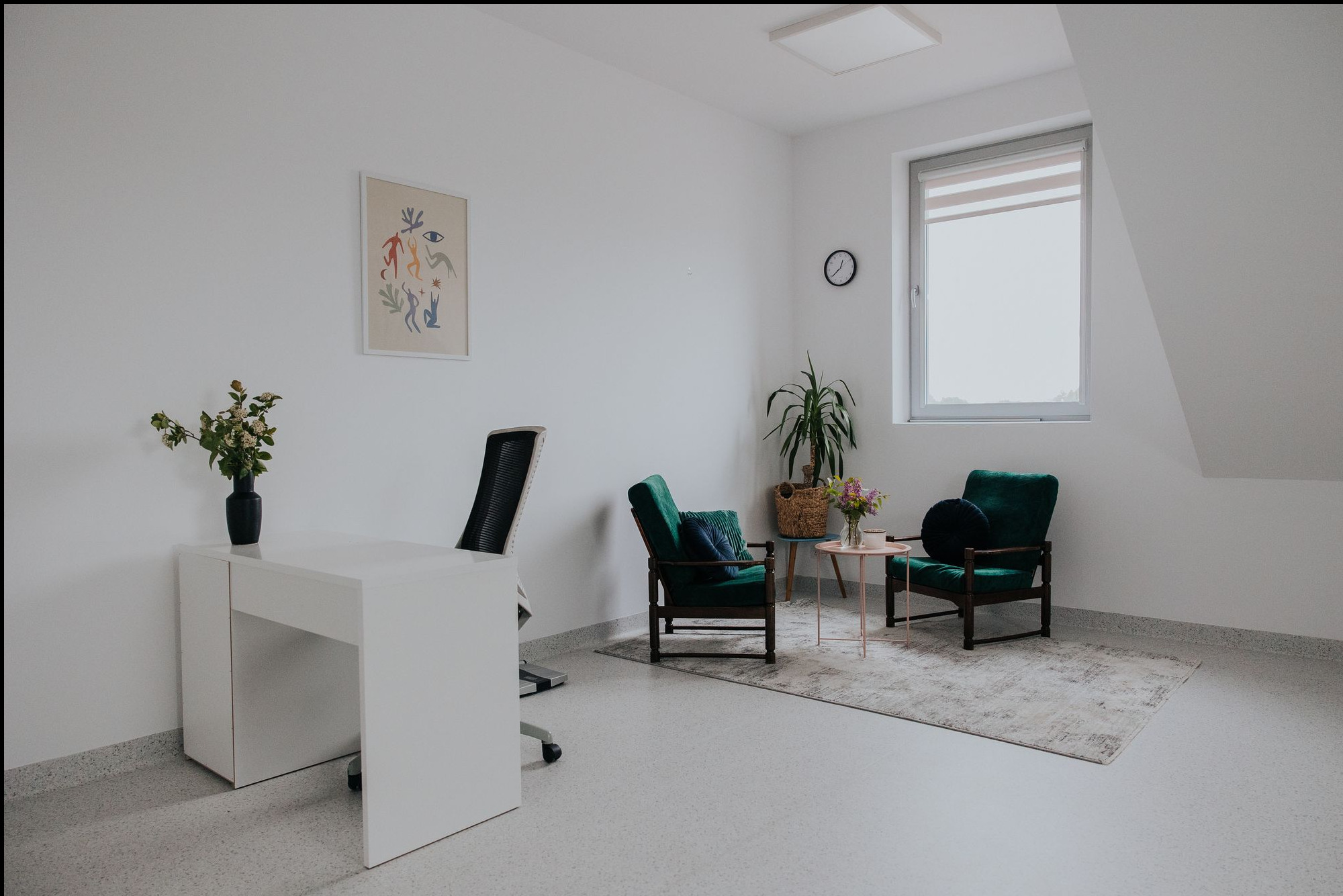 Jasne wnętrze gabinetu z białym biurkiem, zielonymi fotelami, stolikiem kawowym i dywanem, minimalistyczny wystrój z roślinami i abstrakcyjnym obrazem na ścianie.