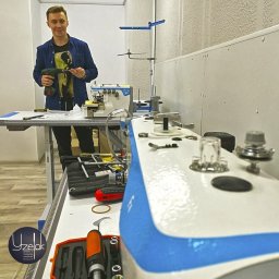 CRAFTUS HANNA YURKEVICH - Mężczyzna z wkrętarką w warsztacie, obok maszyna do szycia, narzędzia i akcesoria na stole.