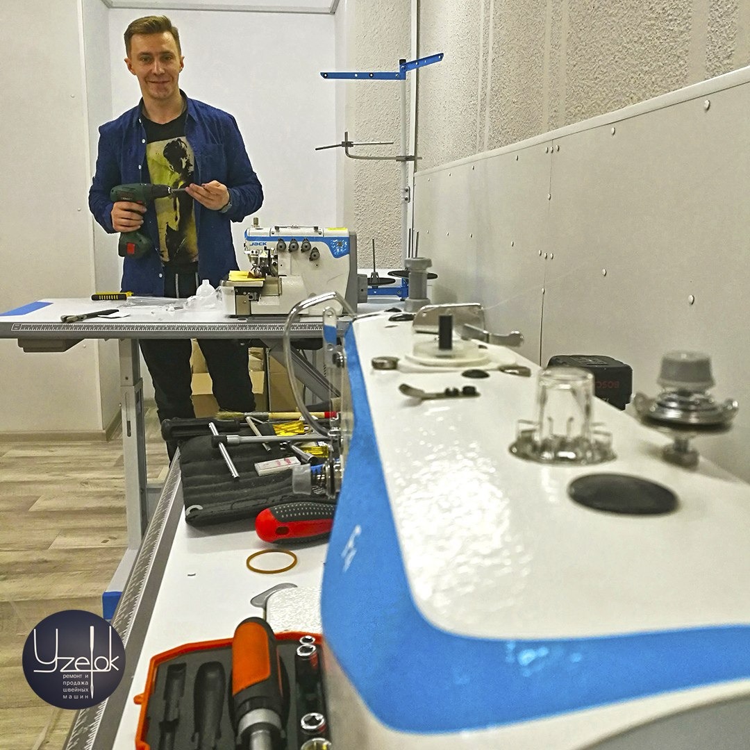 Mężczyzna z wkrętarką w warsztacie, obok maszyna do szycia, narzędzia i akcesoria na stole.