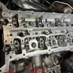 Zdemontowana głowica silnika samochodowego z widocznymi elementami układu rozrządu, oznaczona numerem 'B07', w warsztatowym otoczeniu.