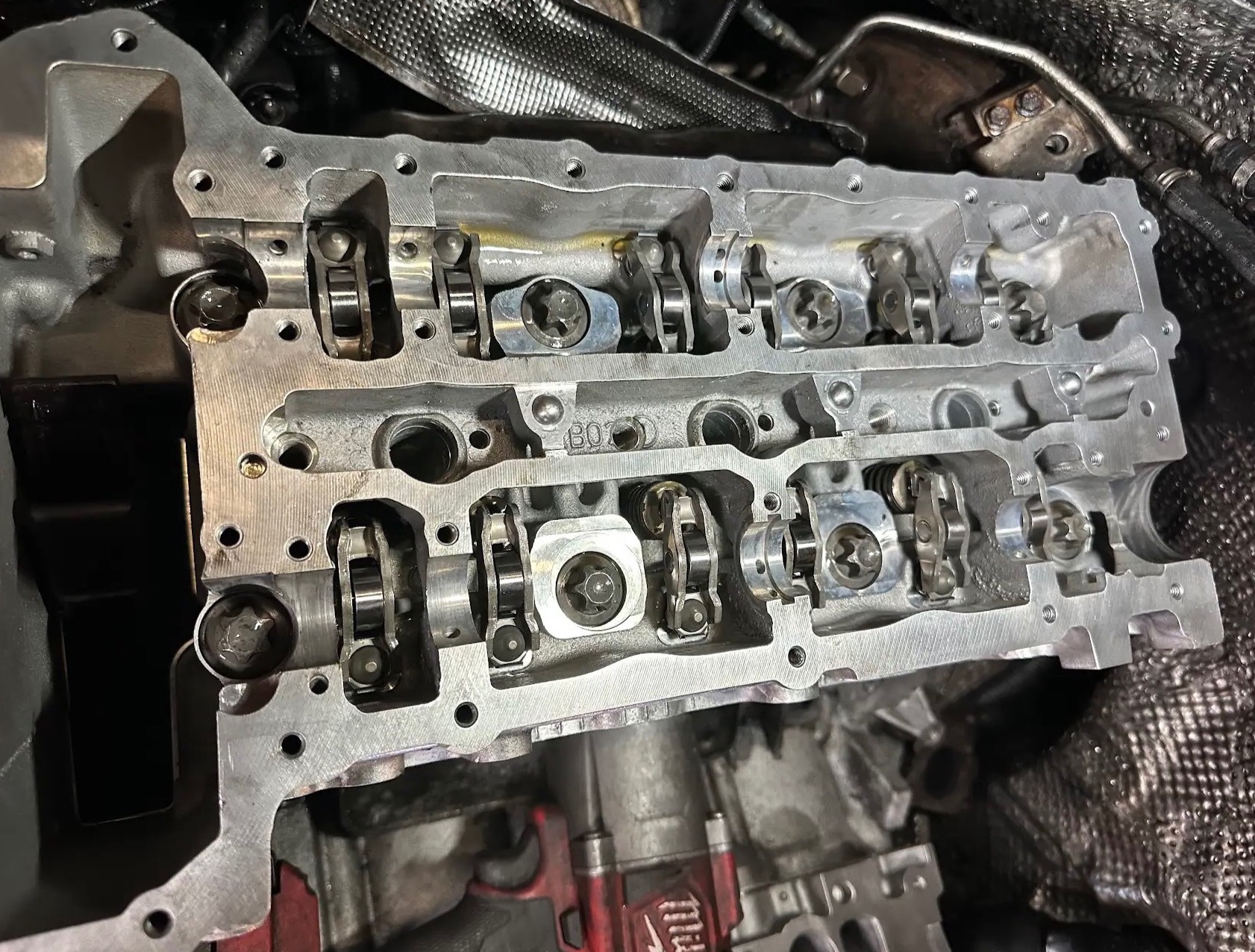 Zdemontowana głowica silnika samochodowego z widocznymi elementami układu rozrządu, oznaczona numerem 'B07', w warsztatowym otoczeniu.