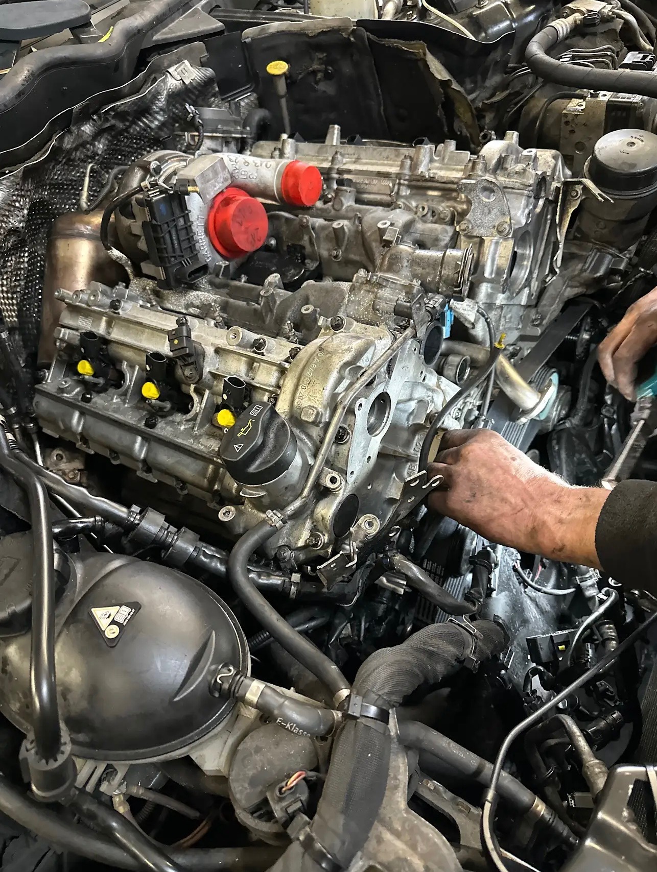 Demontaż głowicy silnika spalinowego z widocznymi turbosprężarkami i elementami układu chłodzenia, ręce pracownika warsztatu w trakcie odkręcania śrub