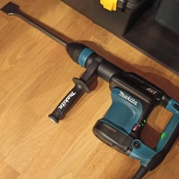 Patryk Pastuszko - Młot udarowy Makita z dłutem płaskim, gotowy do pracy w Krakowie. Narzędzie na drewnianej podłodze, obok skrzynka narzędziowa. Sprzęt do prac rozbiórkowych.