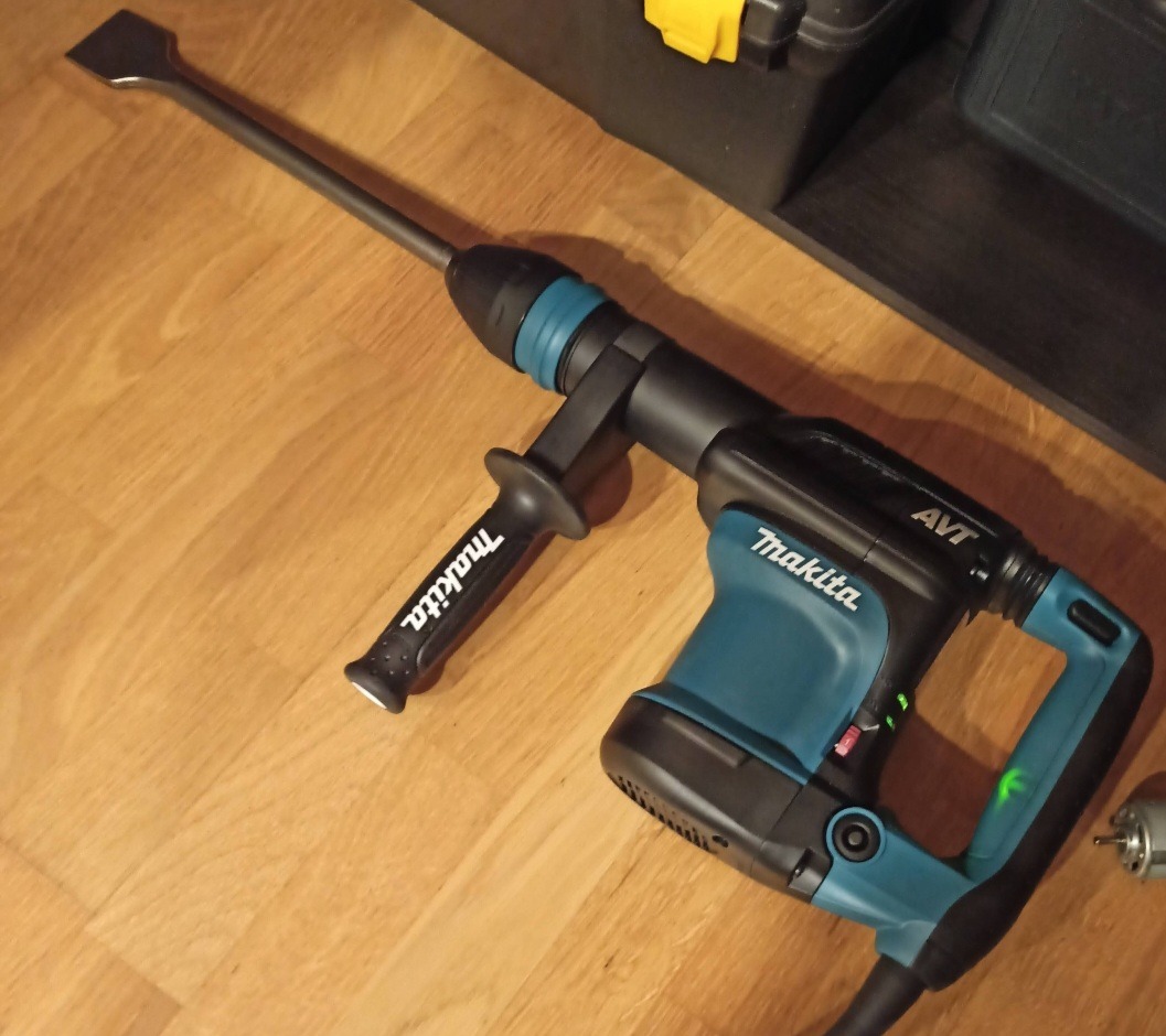 Młot udarowy Makita z dłutem płaskim, gotowy do pracy w Krakowie. Narzędzie na drewnianej podłodze, obok skrzynka narzędziowa. Sprzęt do prac rozbiórkowych.