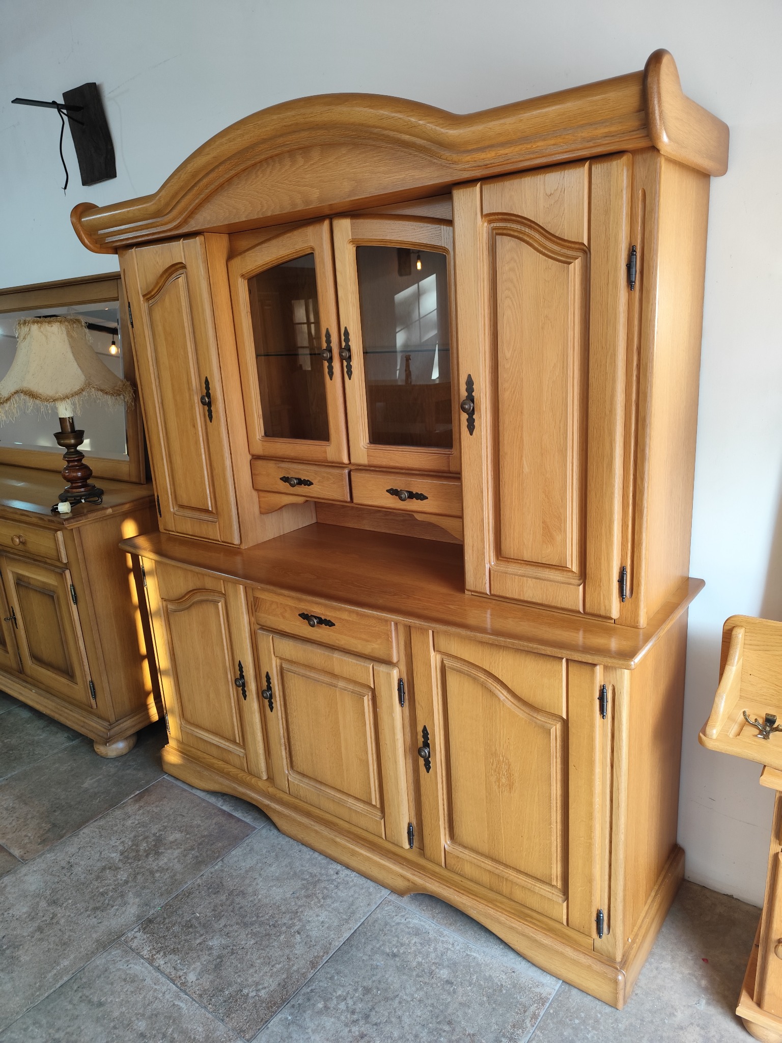 Drewniany, dwuczęściowy kredens z przeszkloną górną częścią, widoczne ozdobne uchwyty i wykończenia w stylu retro.