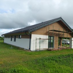 Prywatna - Parterowy dom jednorodzinny z drewnianą elewacją na wysokości dachu, częściowo ocieplony, z rozstawionym rusztowaniem i widocznymi elementami wykończeniowymi.