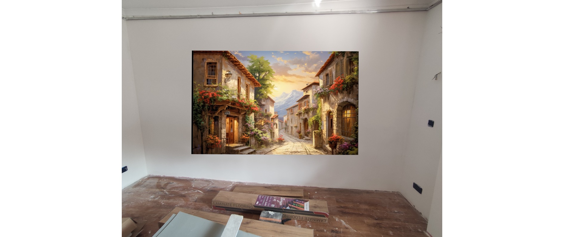 Pokój w trakcie remontu, z położonymi panelami podłogowymi i powieszonym obrazem przedstawiającym włoską uliczkę.