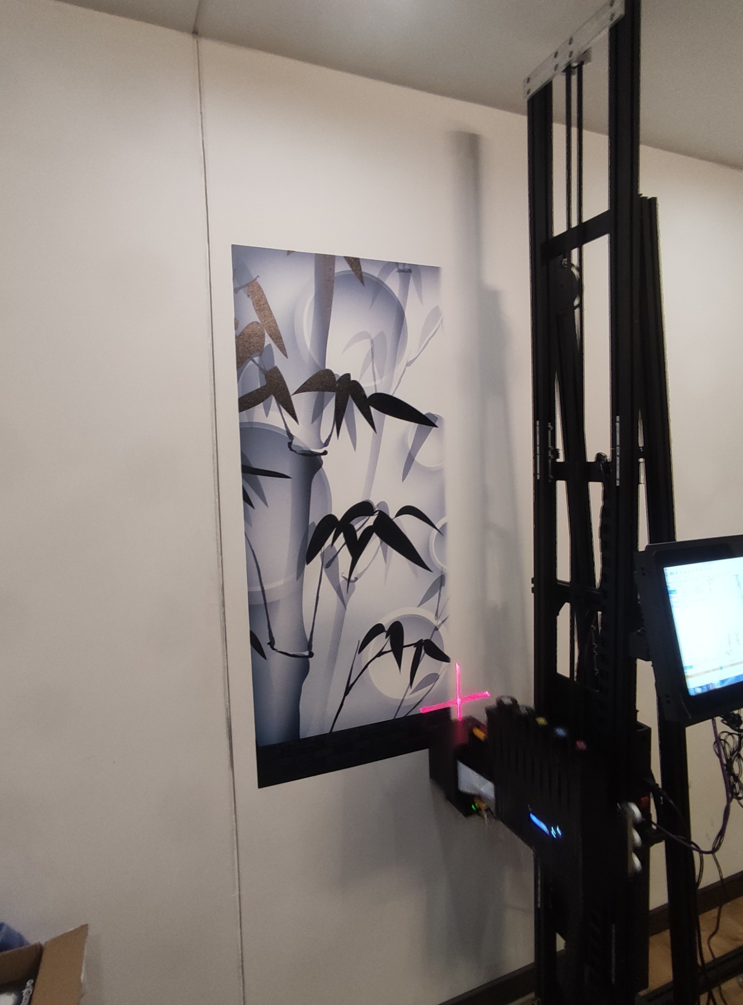 Maszyna do druku pionowego maluje motyw bambusa na ścianie, widoczny laser pozycjonujący.