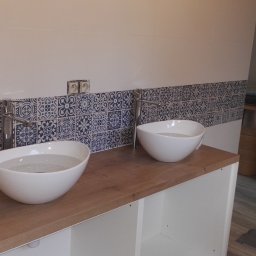 FIRMA REMONTOWO-BUDOWLANA BERT-HOUSE ROBERT KUBACKI - Dwie białe, okrągłe umywalki nablatowe z chromowanymi bateriami na drewnianym blacie. Nad nimi pas płytek w stylu marokańskim. Widoczne gniazdka elektryczne.