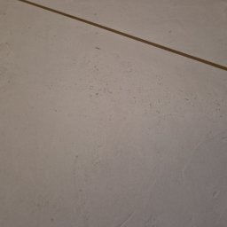 FIRMA REMONTOWO-BUDOWLANA BERT-HOUSE ROBERT KUBACKI - Szara, gładka powierzchnia z delikatną teksturą i widoczną, cienką, brązową linią. Minimalistyczne wykończenie podłogi lub ściany, z bliska, w neutralnym oświetleniu.